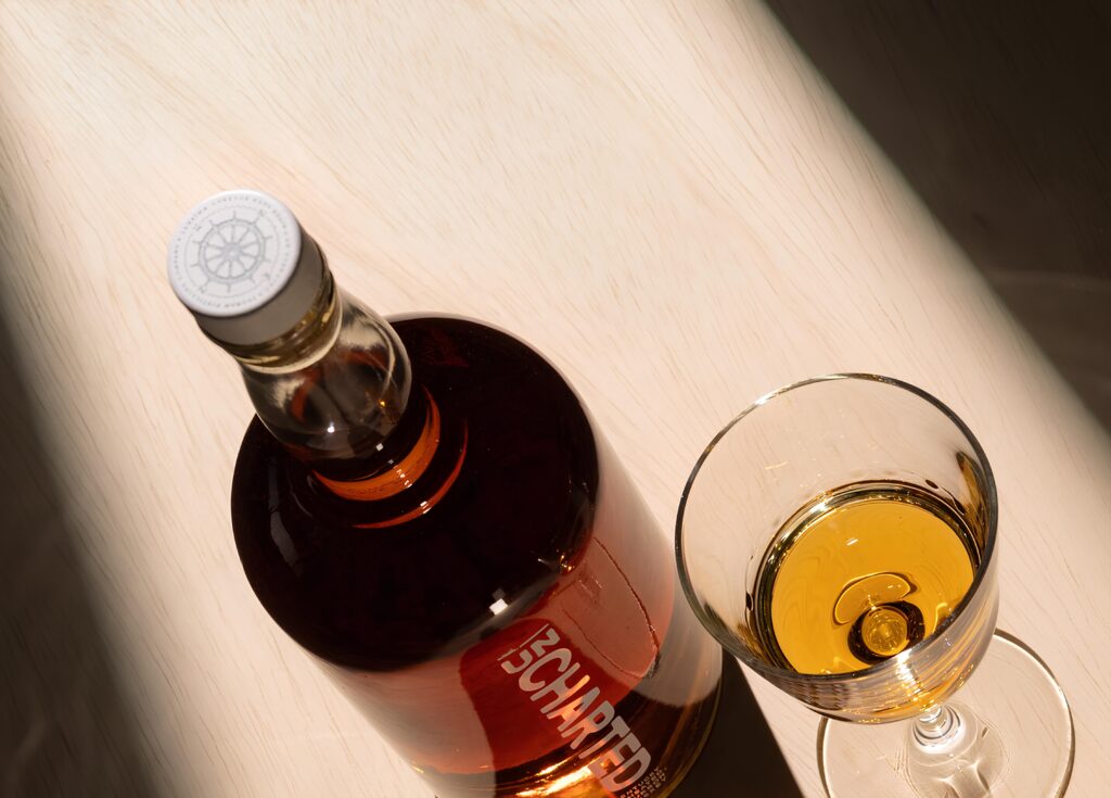 Bouteille de spiritueux haut de gamme avec bouchon en liège et capsule personnalisée, accompagnée d’un verre contenant la même boisson.